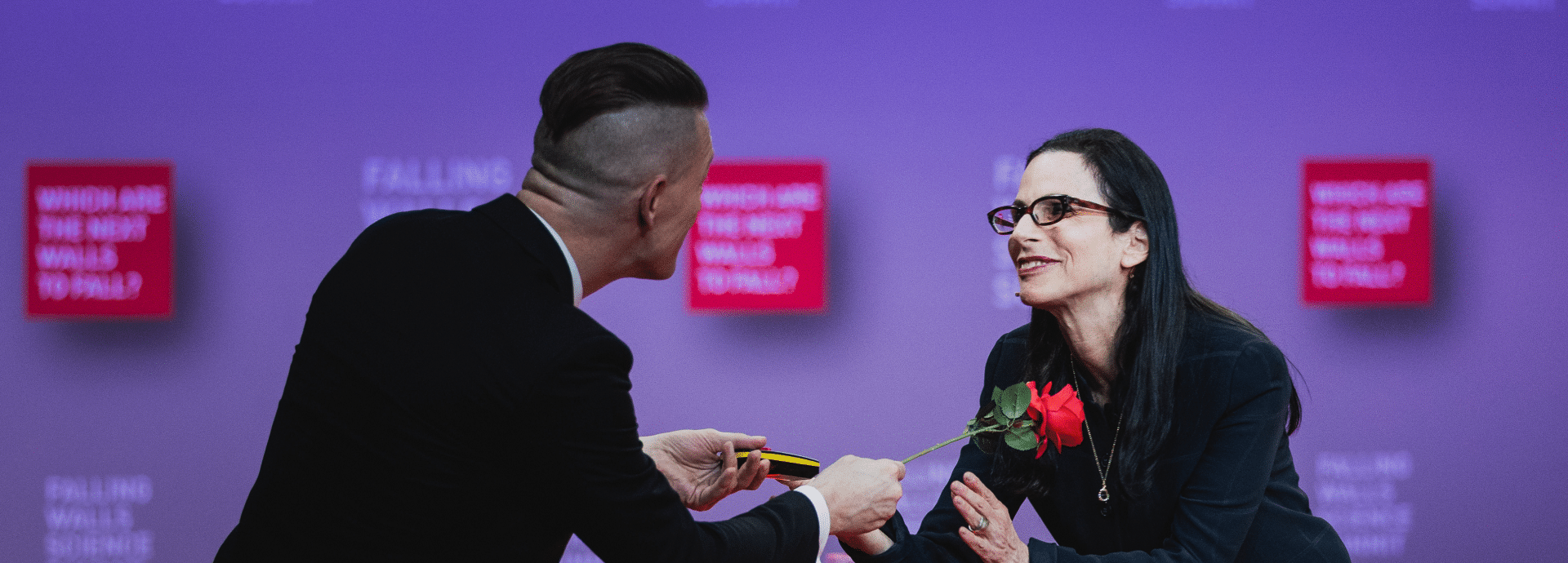 A man gives a single flower to a speaker at the Science Summit stage.