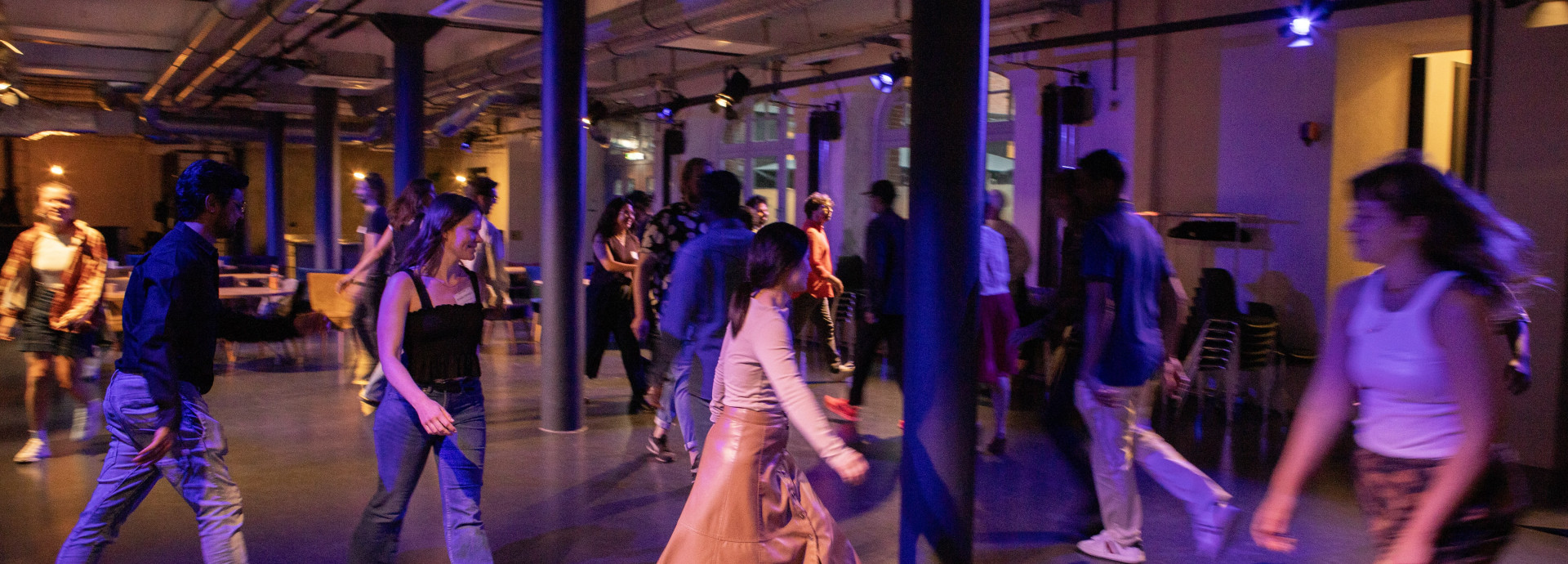 Workshop participants moving around a room with dim purple lighting 
