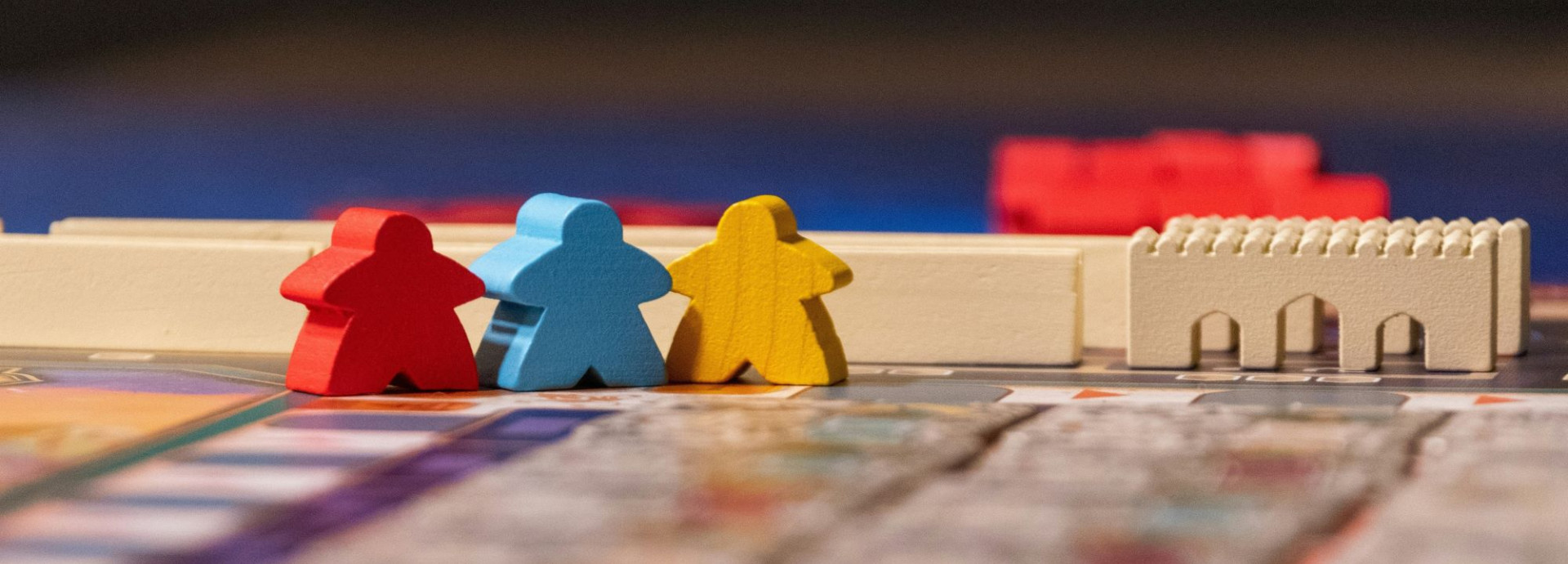Image of board game with wooden player pieces in red, blue and yellow