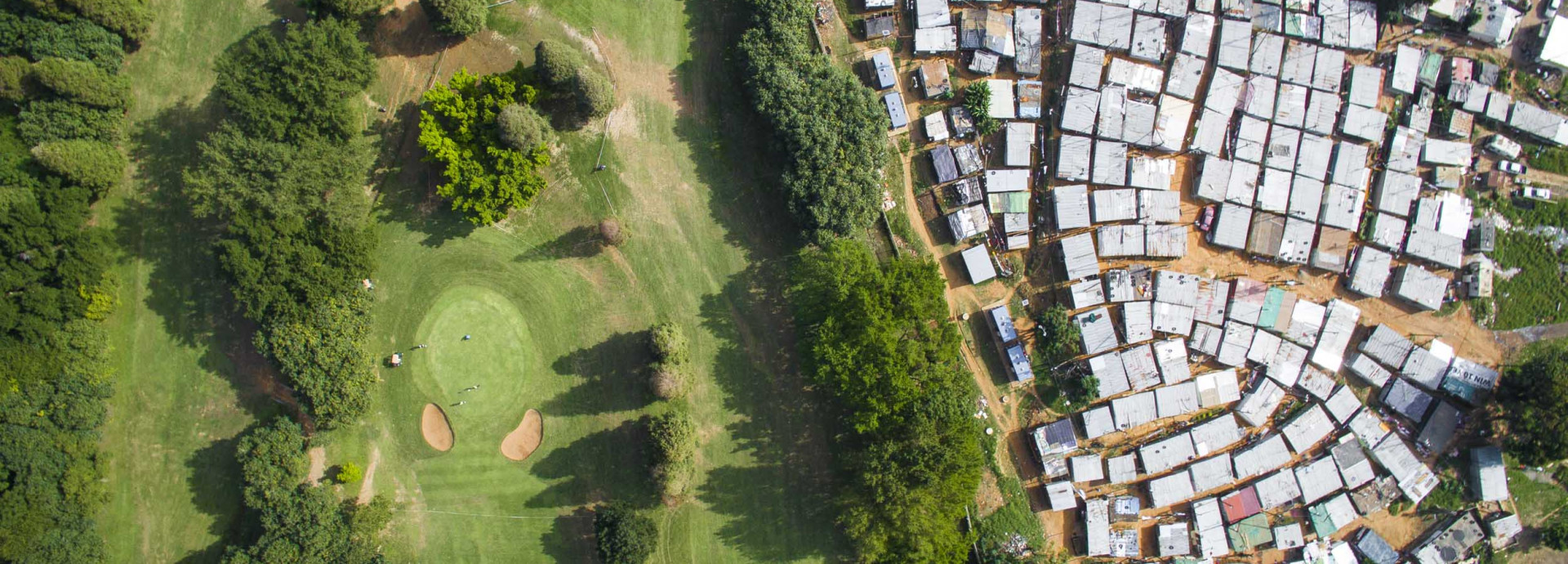 A green golf course with a sprawling informal settlement next to it. 