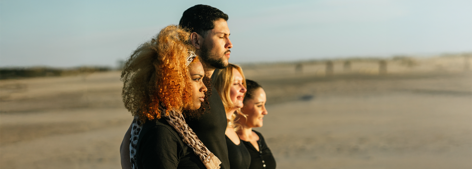 Four people standing and looking at the horizon, with a beach in the background