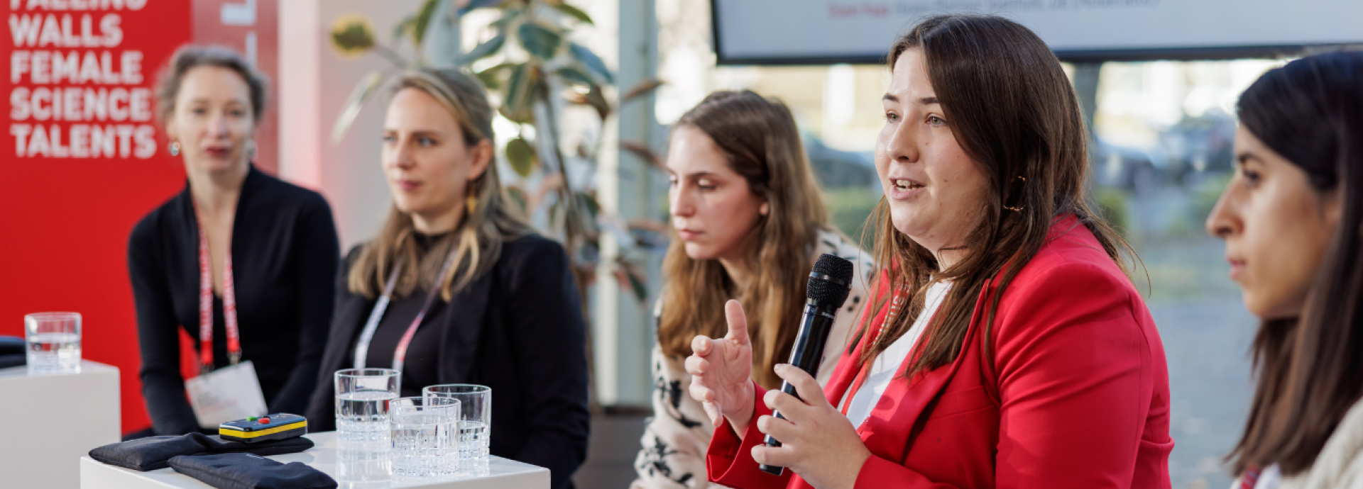 A group of five women scientists are sitting in a row. The second woman from the right is speaking. Everyone is listening to her.