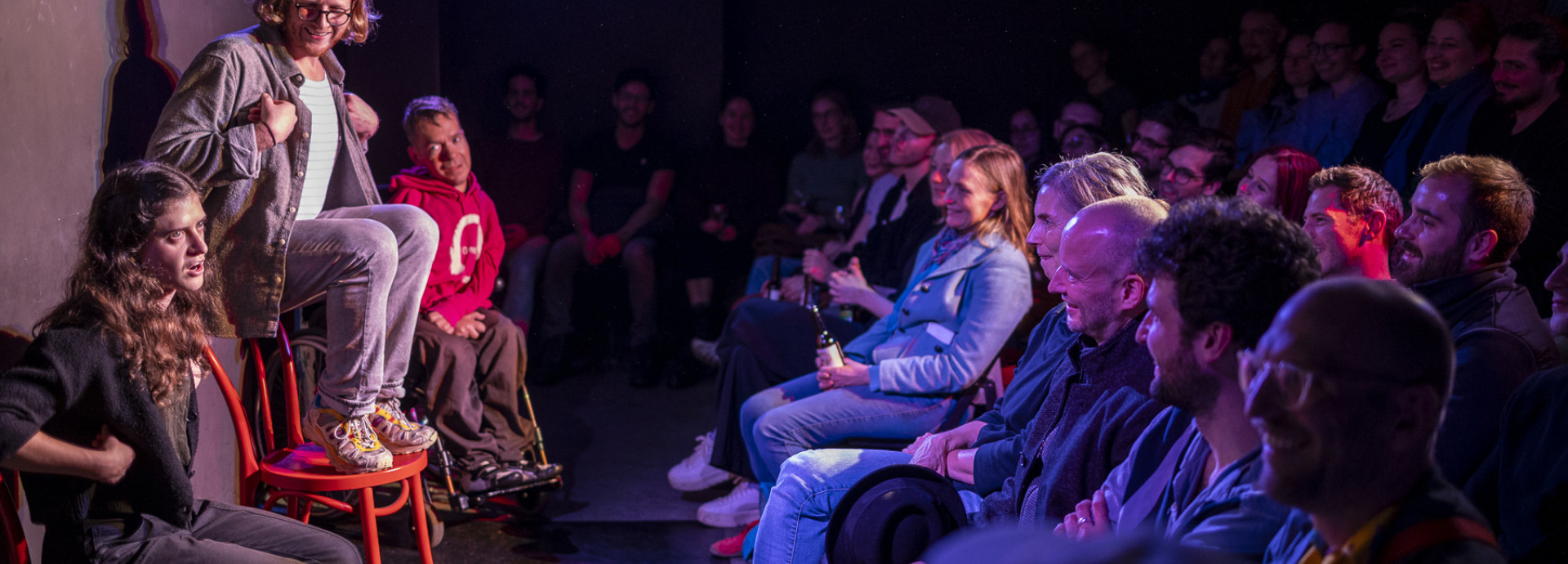 Three performers impersonate birds on stage with audience laughing.
