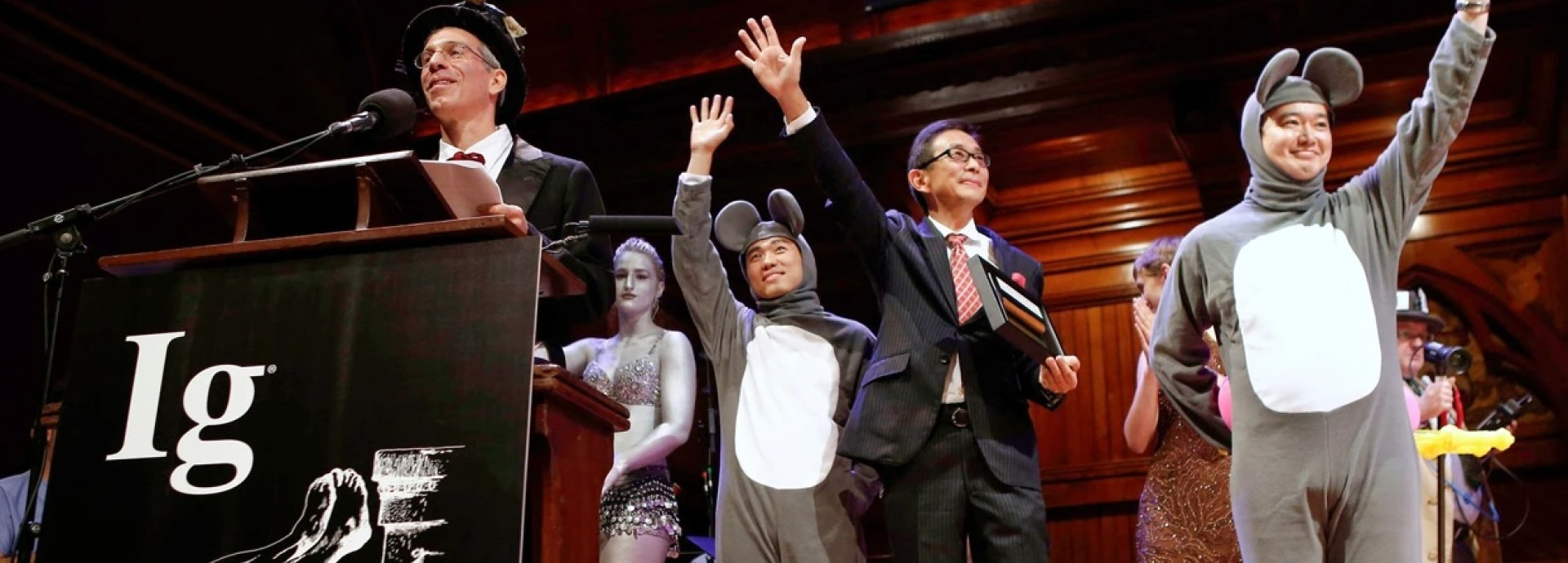 Marc in top hat at podium alongside men dressed as mice and women in silver paint.