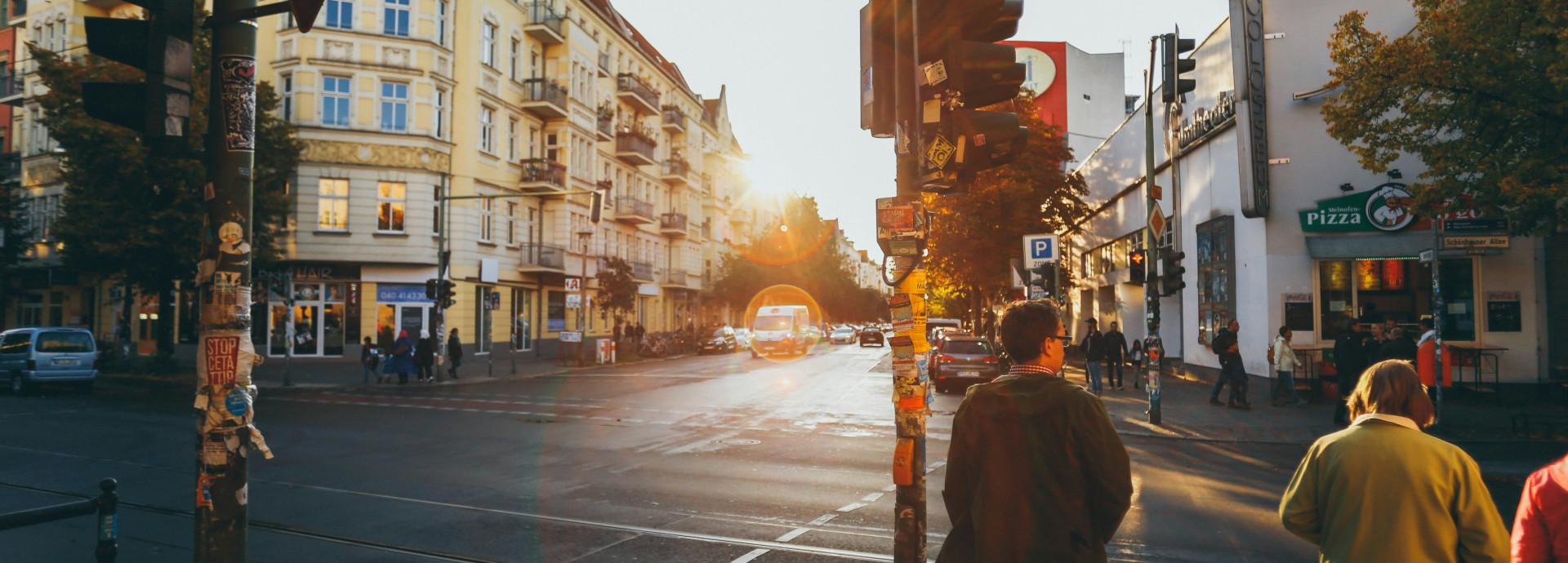 Straßenszene an der Schönhauser Allee mit Fußgängern an einer Ampel und Gebäuden im Hintergrund bei Sonnenuntergang
