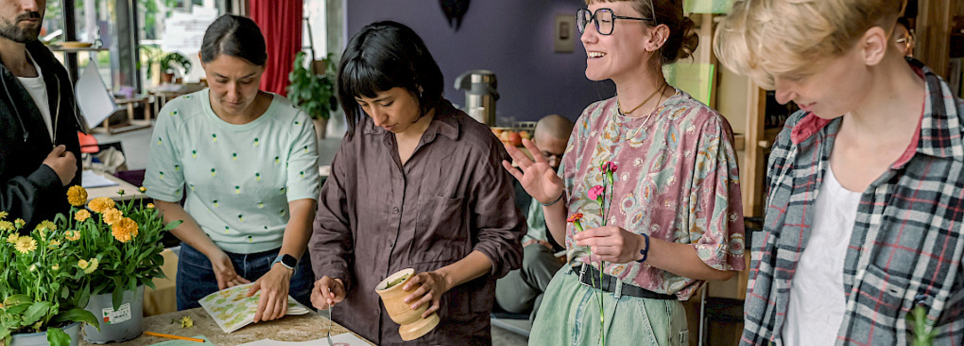 Participants work at a table covered in plants and flowers during a hands-on workshop at SAVVY Contemporary, Berlin.