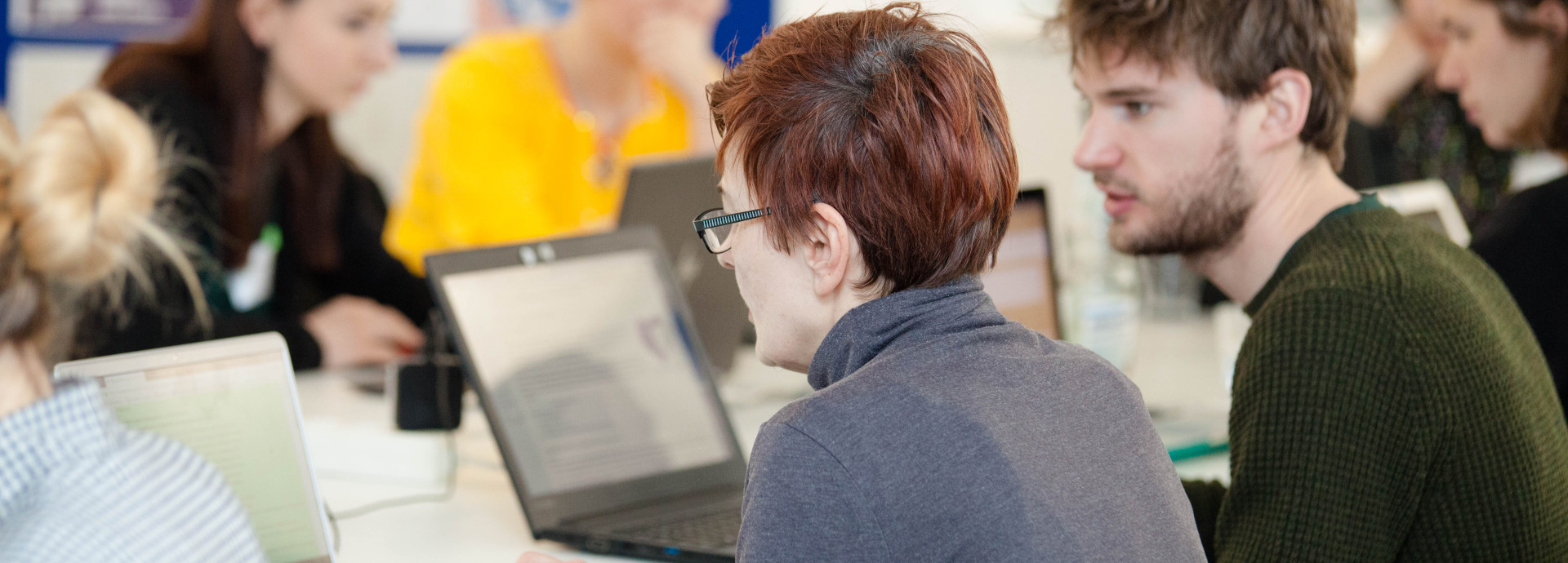 a group of different people in front of computers talking to each other and writing 