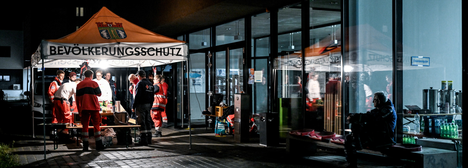 Zelt mit der Aufschrift "Bevölerkungsschutz" auf einer dunklen Straße neben einem schwach beleuchteten Gebäude. 