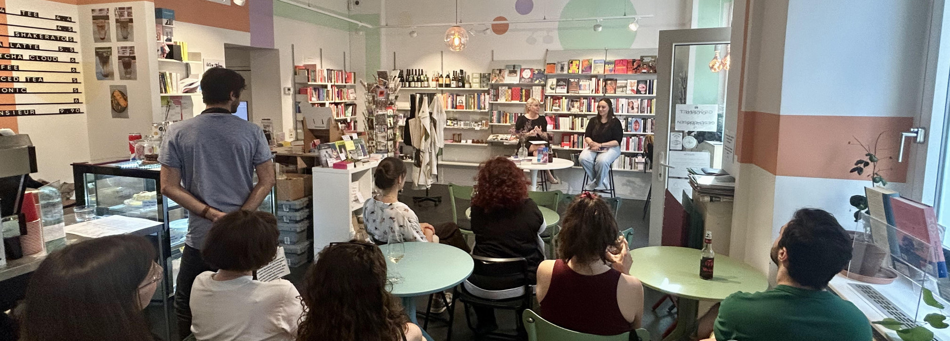 A group of people sitting down around tables, with their backs to the camera, in a book store, listening to a talk