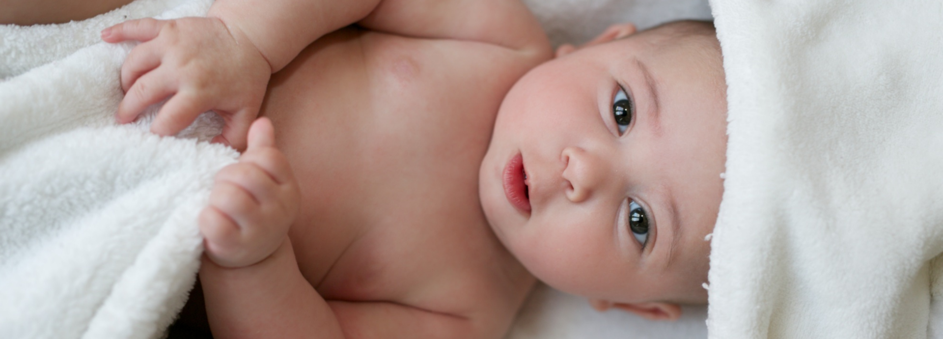 Ein Baby wurde in  ein Handtuch gewickelt und schaut in die Kamera.