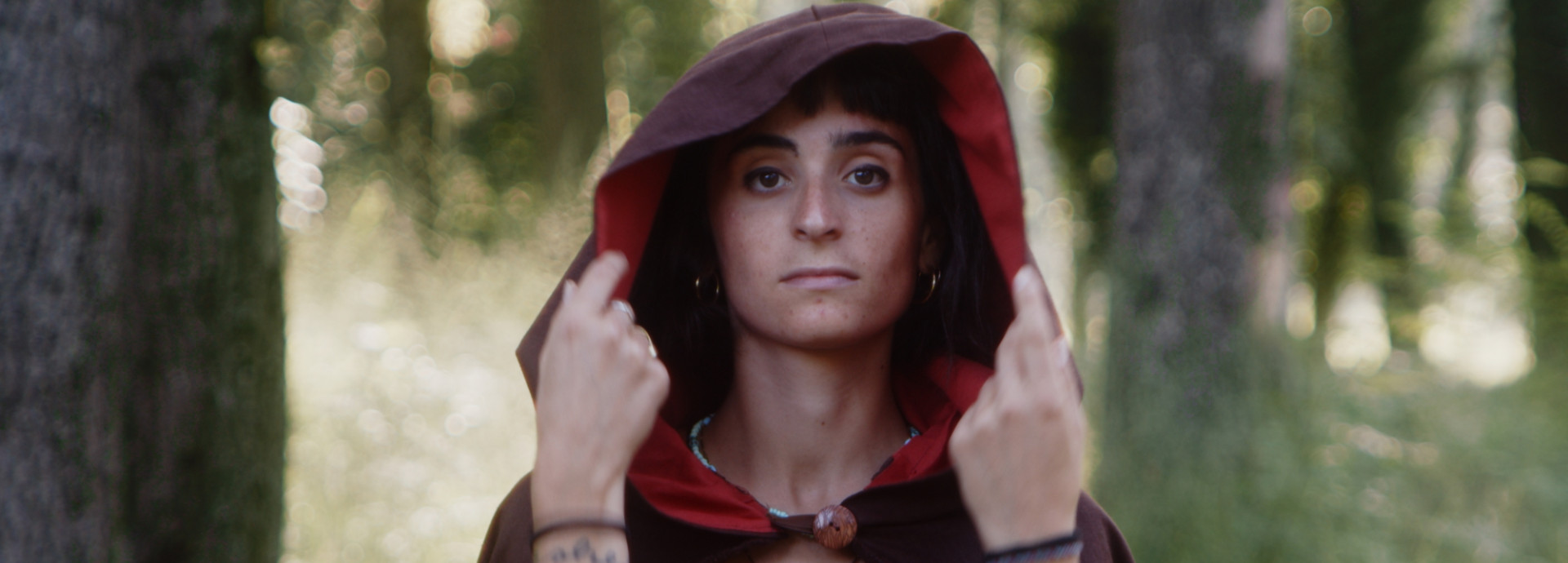 Head and shoulders of a woman in a red hooded cloak with out of focus forest in the background