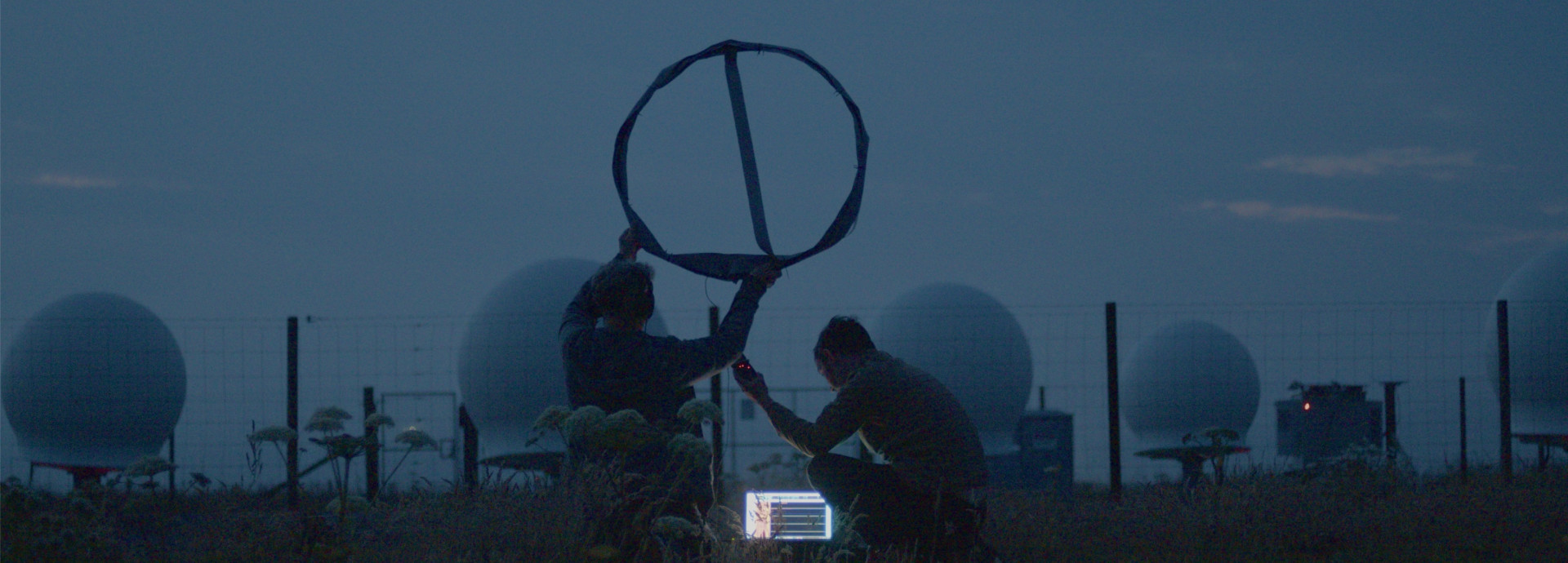 Image from Song for the Cosmos showing artist Edwin Mingard and musician Gina Ritch at dusk, listening to a spaceport's ground control using an experimental aerial
