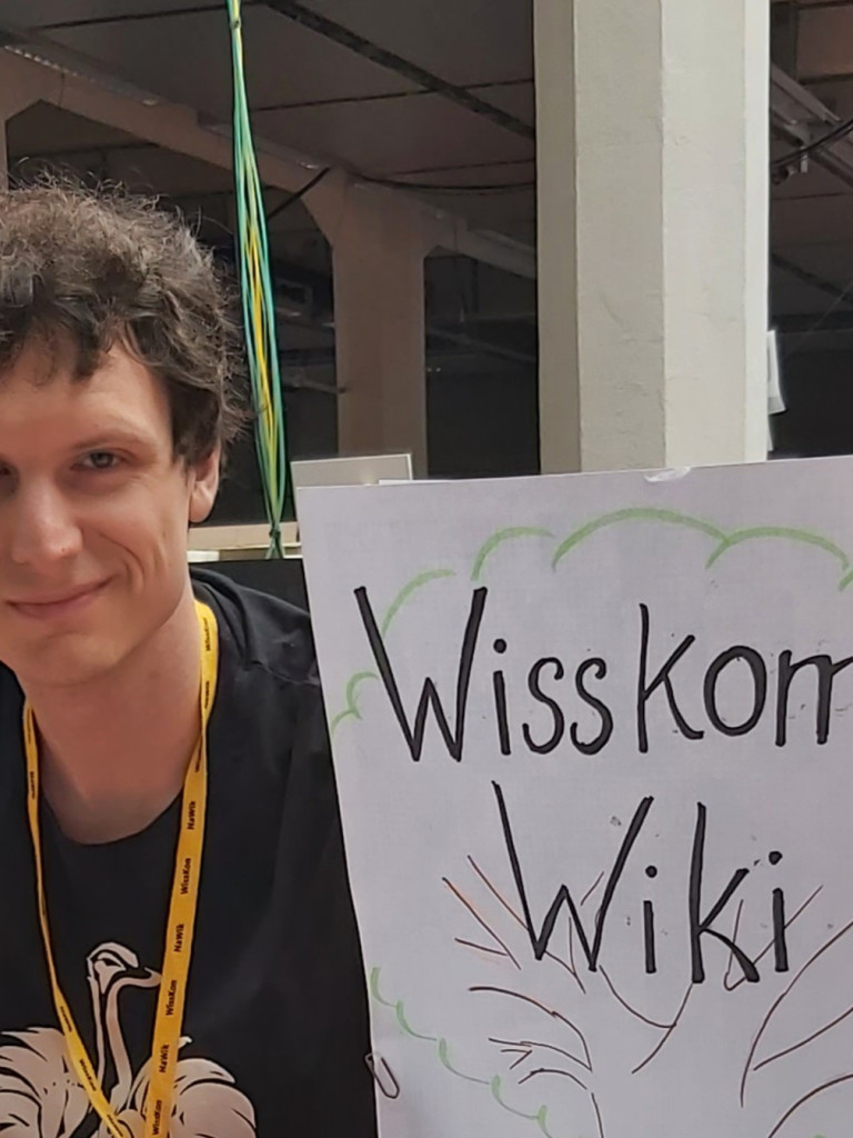 A person in front of a window next to a huge paper showing the text "WissKomm Wiki" in a sketched tree
