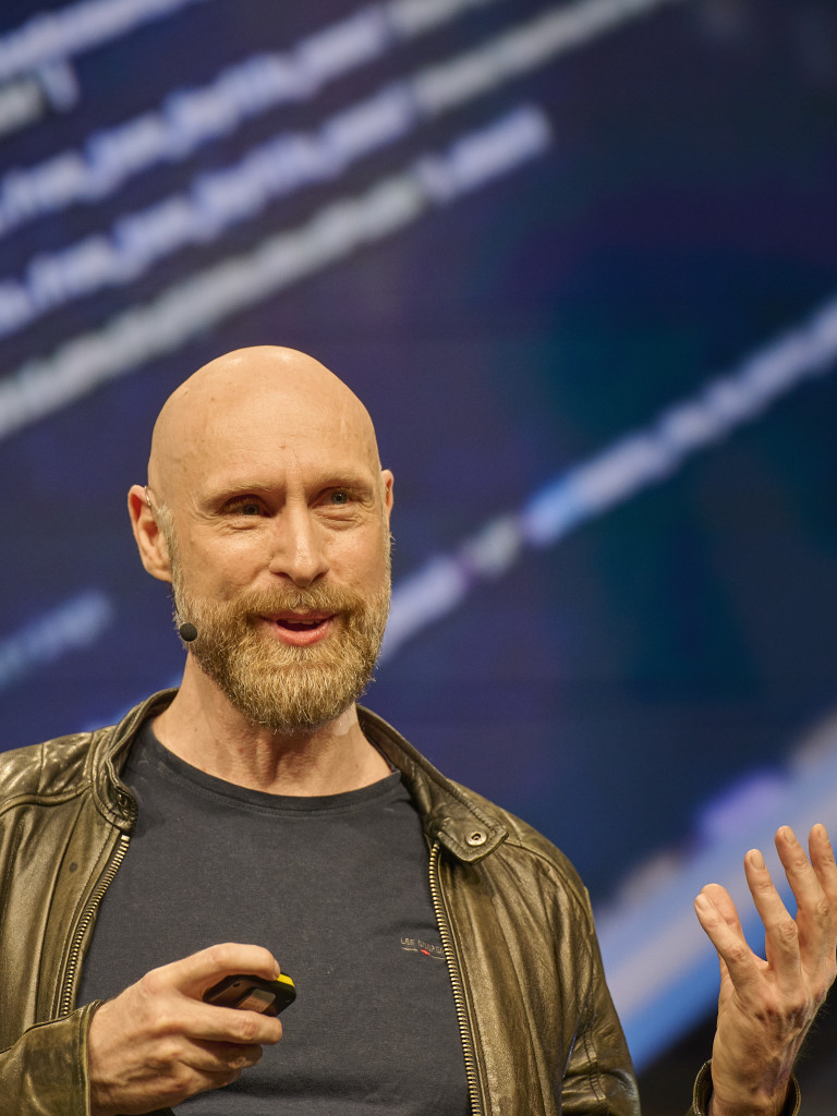 Artist Roman Lipski presenting on stage in front of a screen displaying code.
