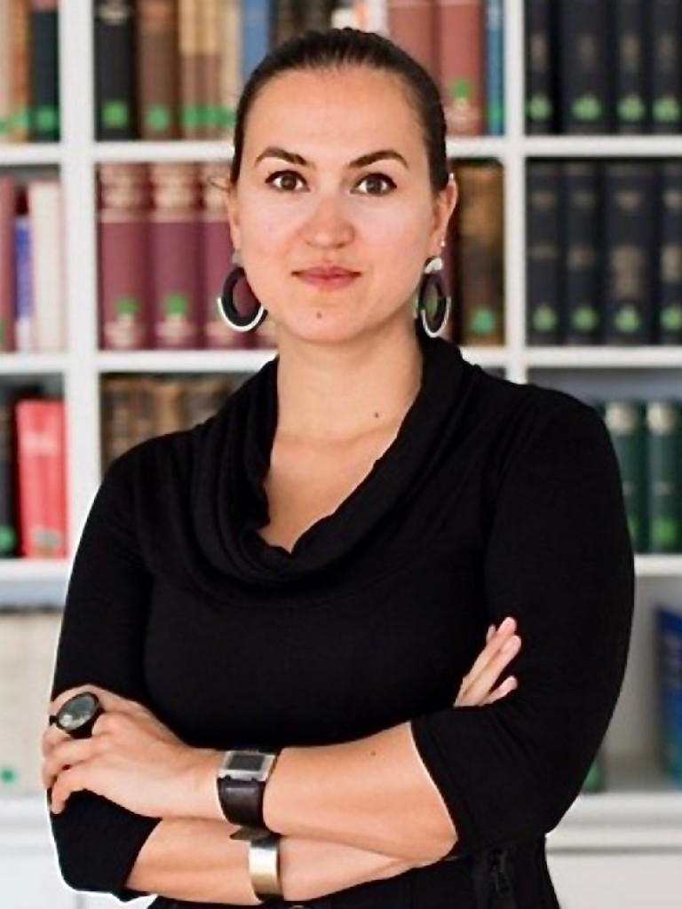 Person with crossed armes in white shirt in front of a book shelf.