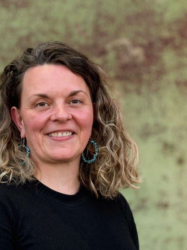 Dr. Christien  M. Beez wearing a black sweater, smiling at the camera