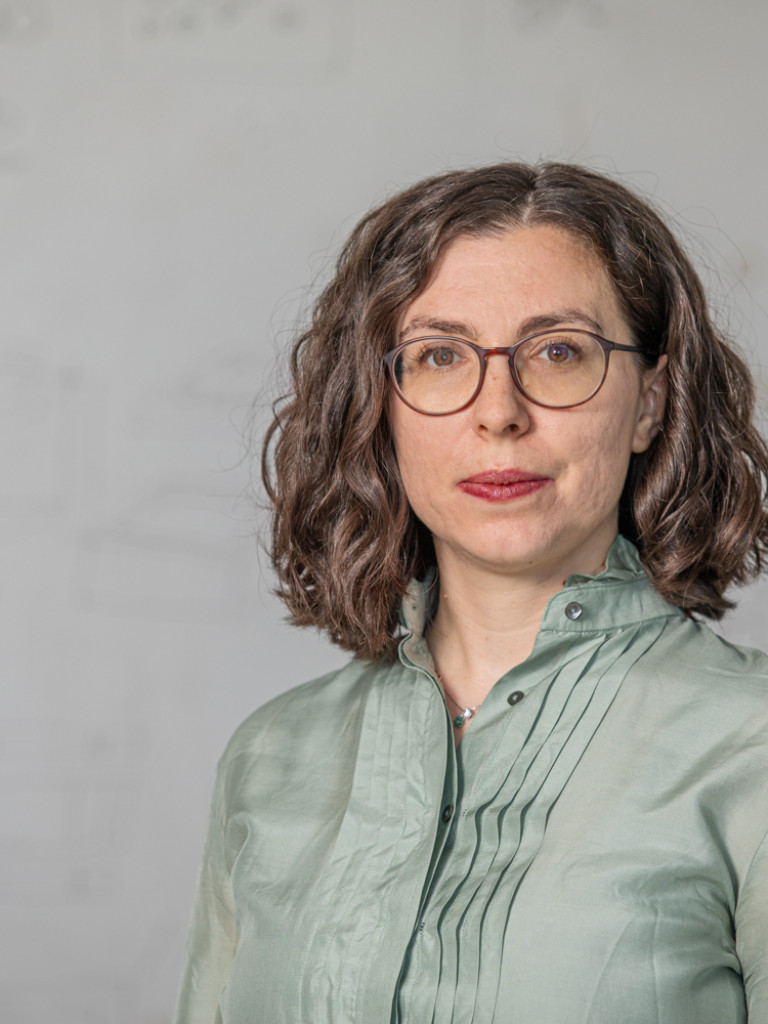 Dr. Laura Zorzetto wearing a green blouse and glasses in front of a light grey background.