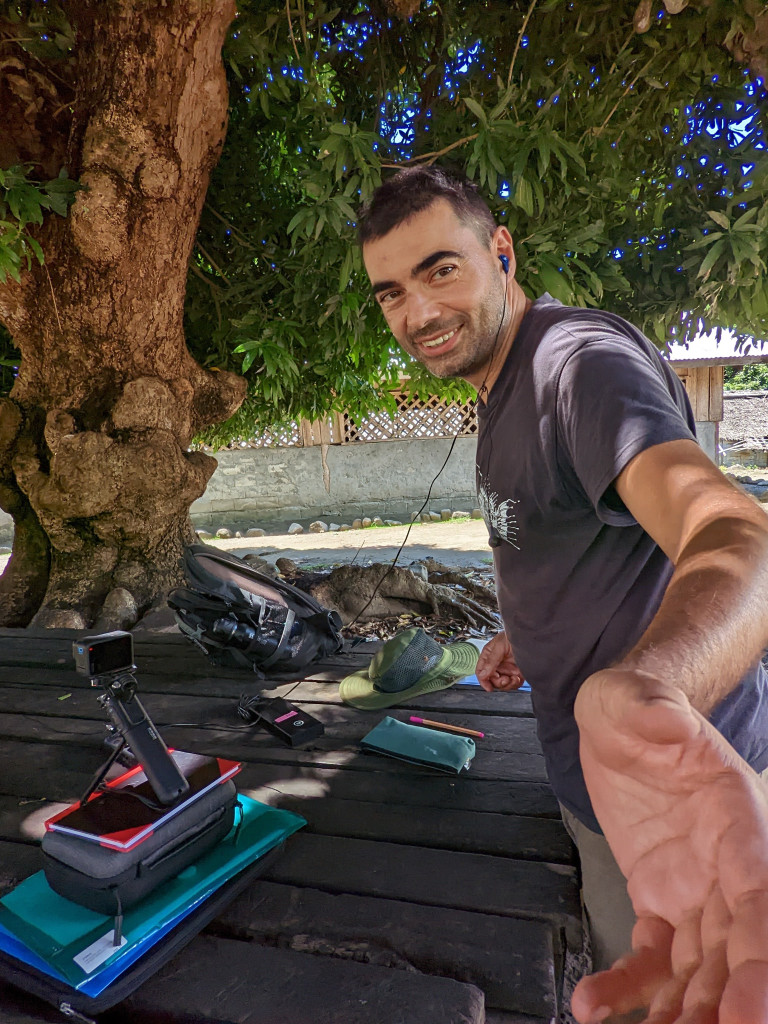 Tihomir is smiling at the camera while wearing earphones. He has a small camera pointing at a man, who is also wearing an earphone.