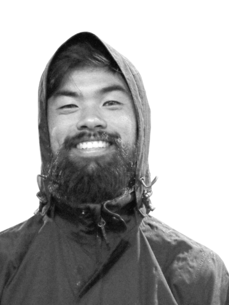 Black and white portrait of an Asian man smiling with a beard, wearing a rain jacket.