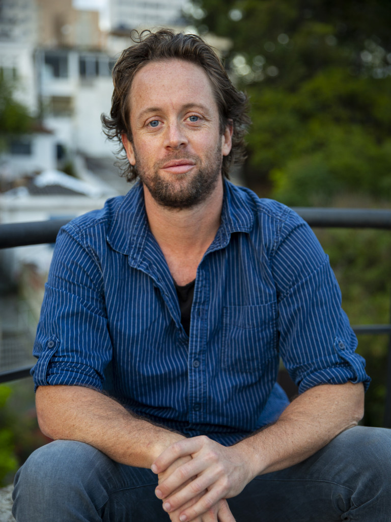 Johnny Miller sitting looking at the camera in a blue shirt and jeans.