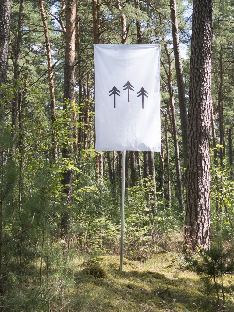 Vertically oriented white flag displaying an illustration of three black trees amidst a lush green forest.