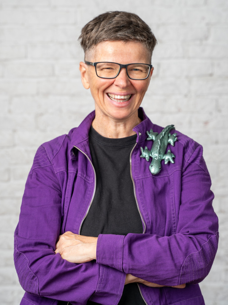 Portrait of person with purple jacket and lizard toy on shoulder.