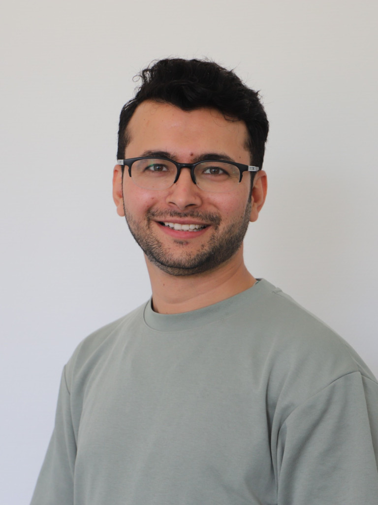 A young man with glasses and black hair and beard smiling