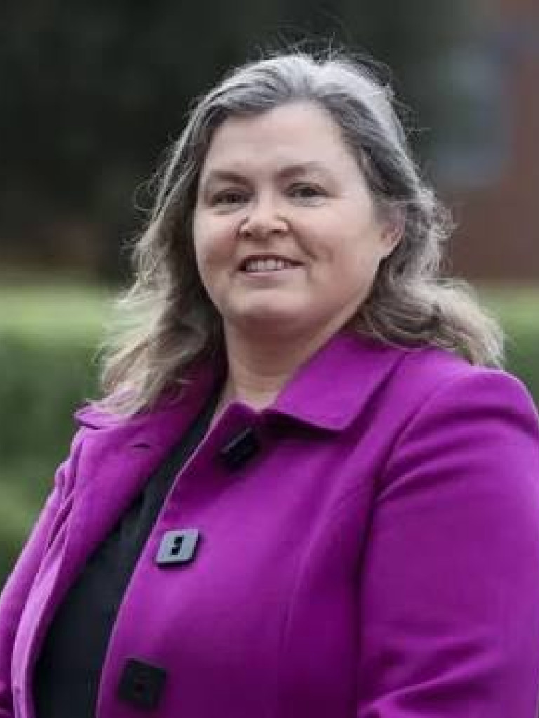 Woman with long hair in purple coat stand and smiles. 