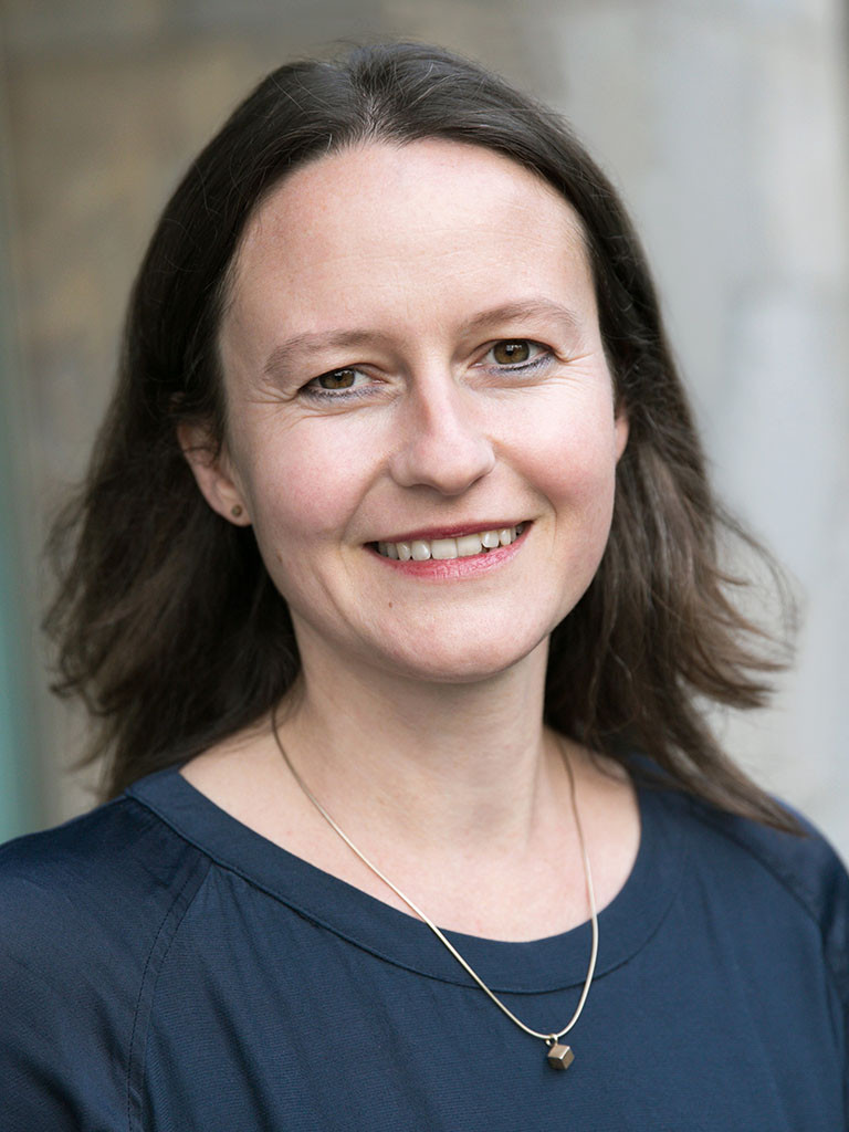 Portrait einer Frau, sie hat langes braunes Haar und trägt ein dunkelblaues Kleid.