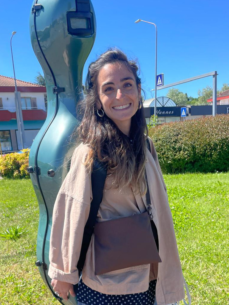 Image of Caterina Cacciatori framed by blue sky and carrying her cello case on her back