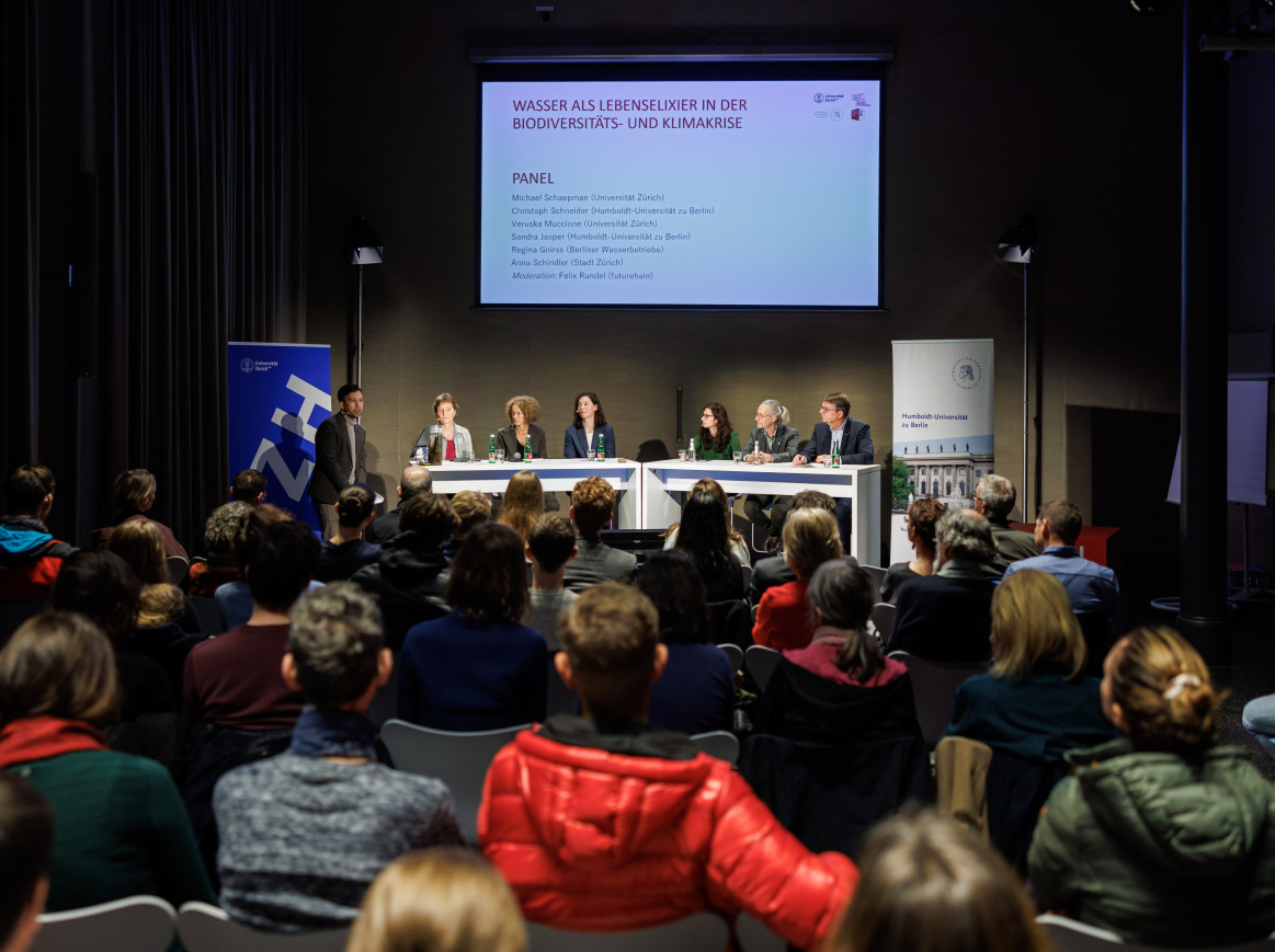 A crowd sits in front of a panel discussion with a big screen. 