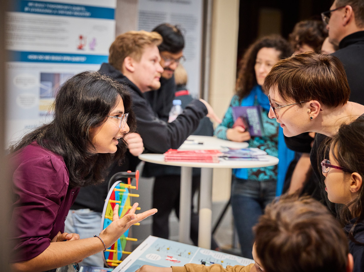 A woman leans over a table to speak to another woman. 