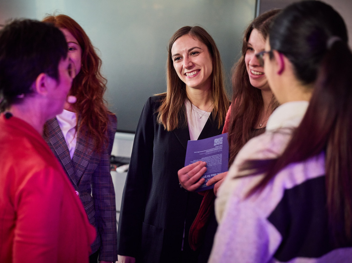A group of women smile at one another. 