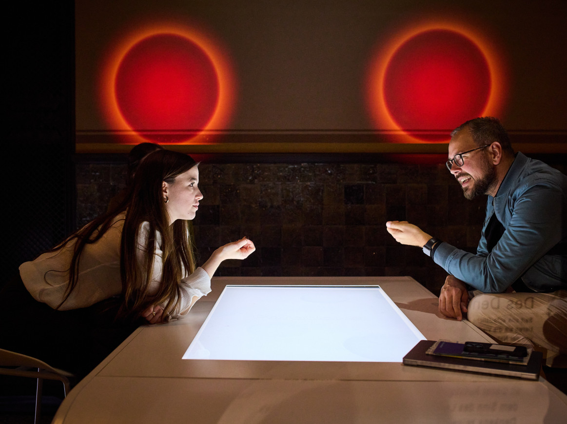 Two people sit over a glowing table with glowing orbs above their heads. 