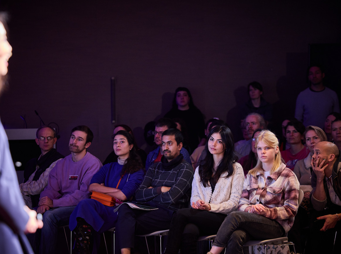 Two women look at a speaker on a stage. 