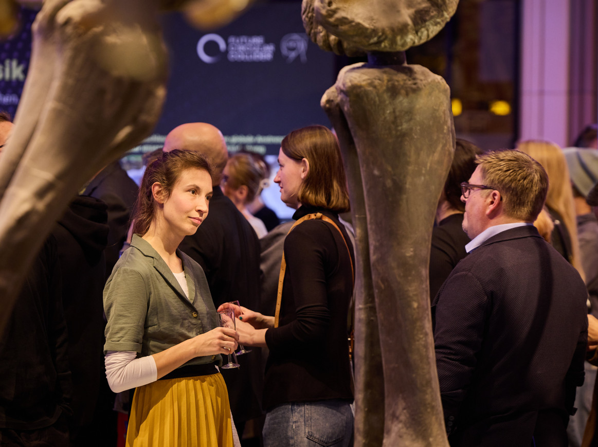 A woman stares into the distance, framed by dinosaur bones in a museum. 