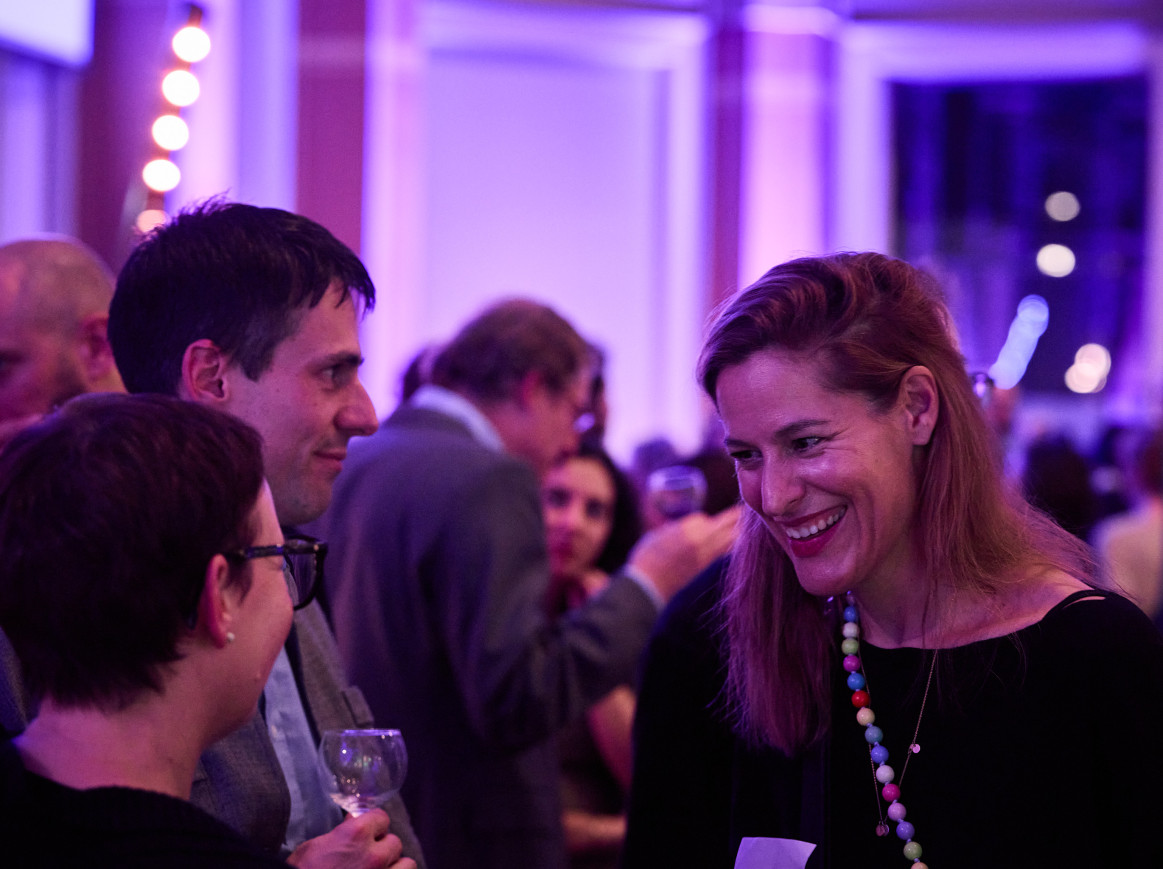 A woman smiles and laughs at another at a networking event. 