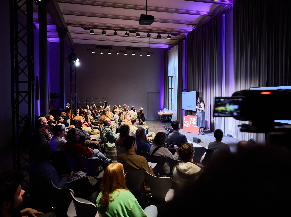 A full room with a woman on stage. 