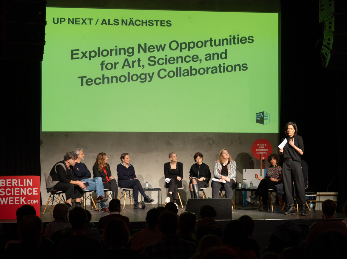 A group of people sit on a stage with a big screen behind them