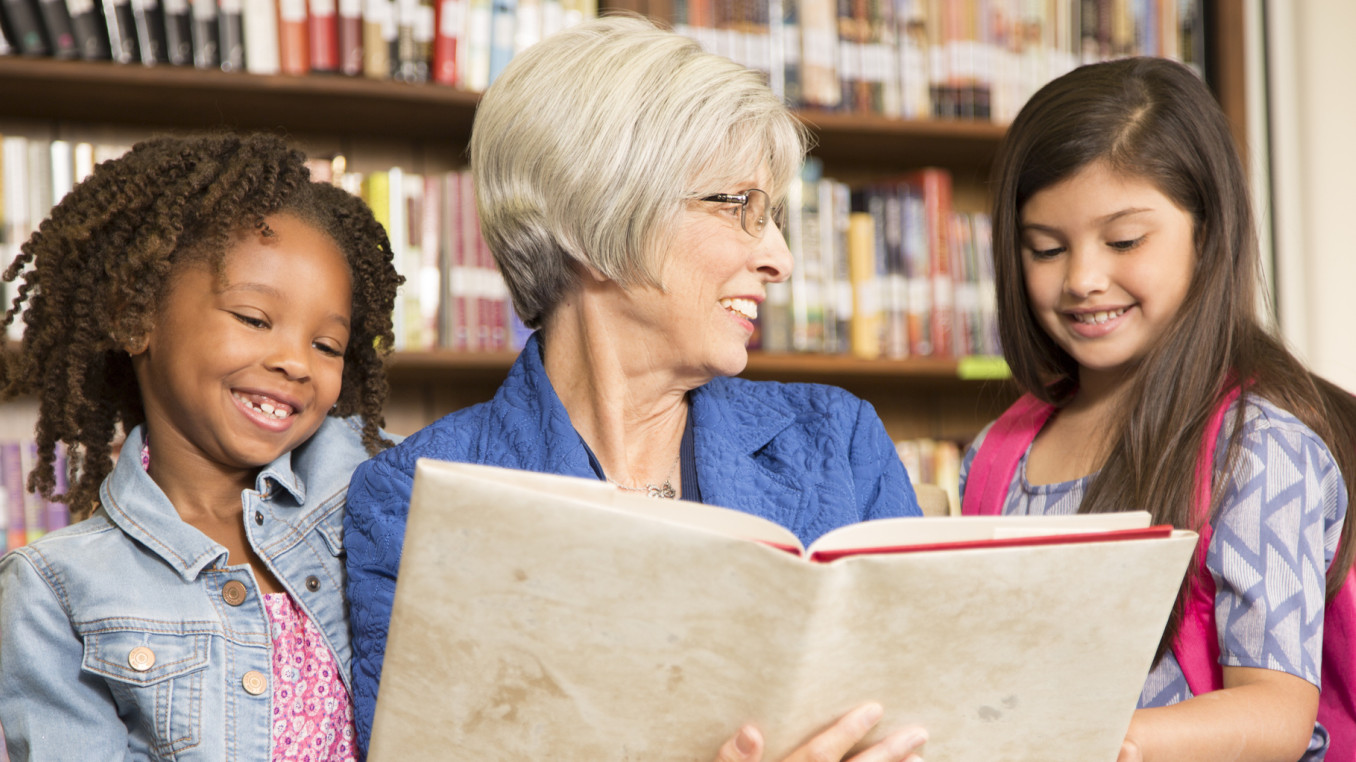 Frau liest zwei Kinder aus einem Buch vor