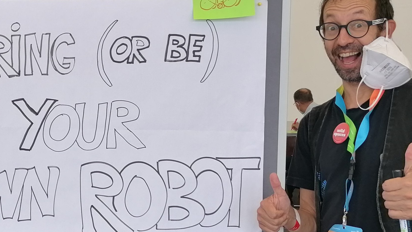 TeeKay neben einem Schild: Bring your own robot !  Bring Deinen eigenen Roboter mit