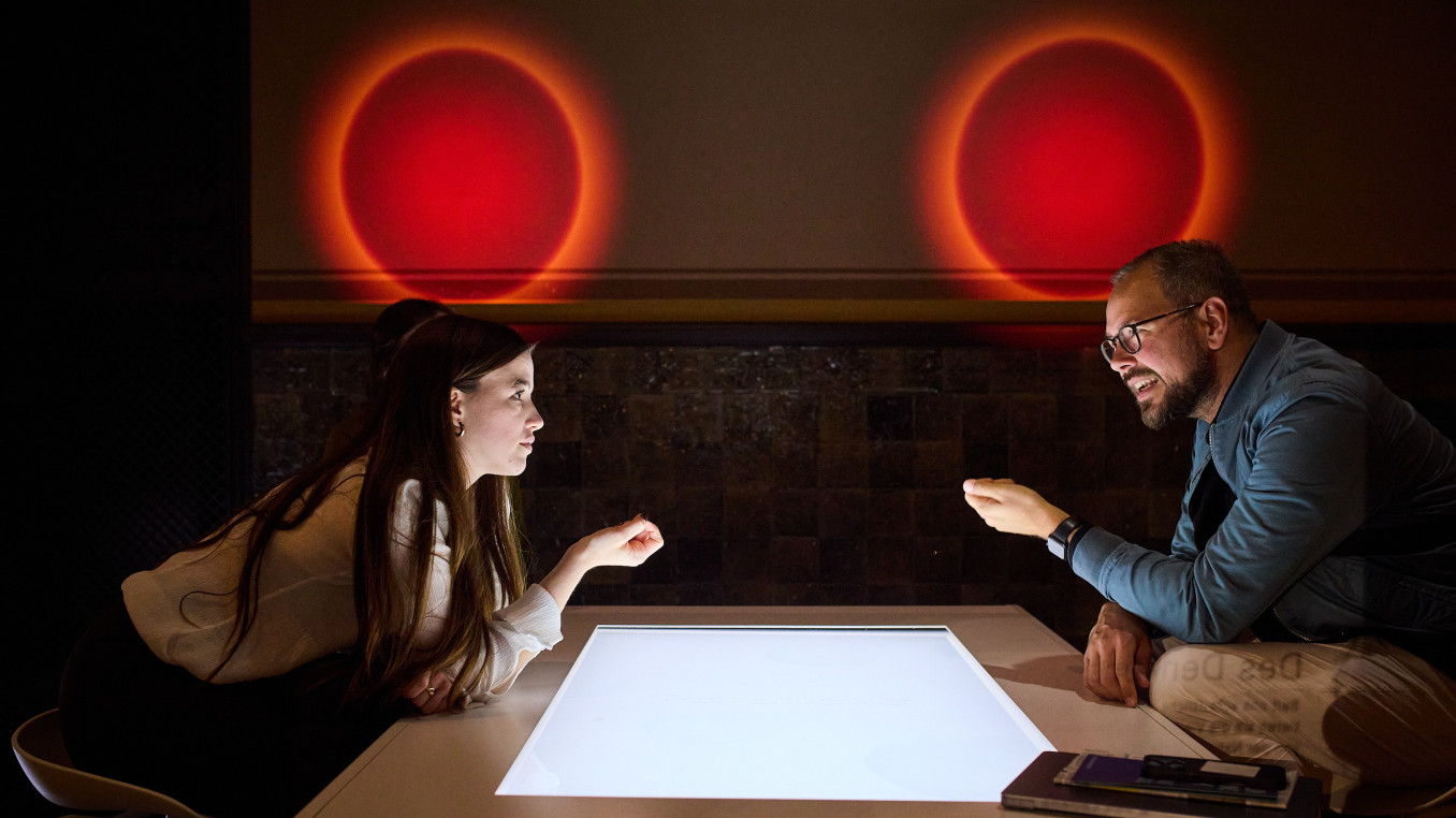 Two people speaking over a table with red orbs over their heads