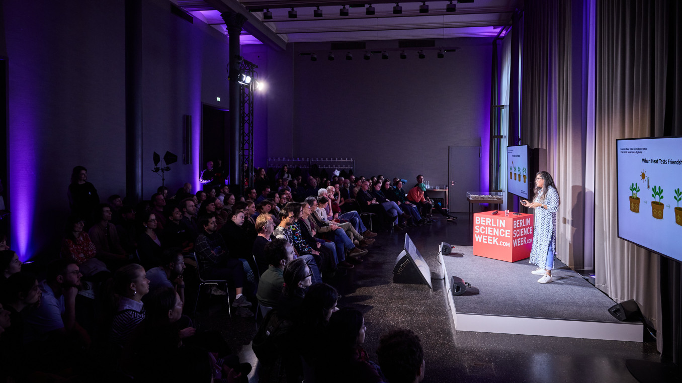 A woman stands on a stage sharing her research about plants. 