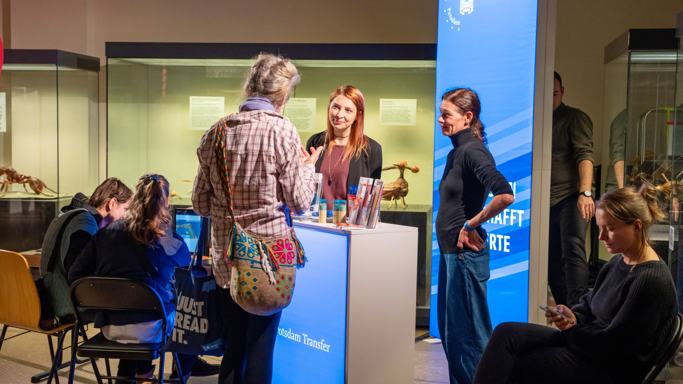 Scientists stand at an exhibition stand with a woman asking questions.