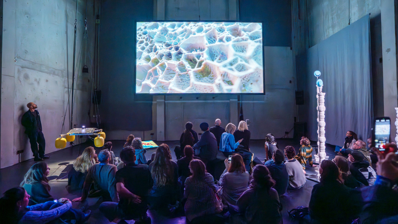 A group of people staring at a big screen above them. 