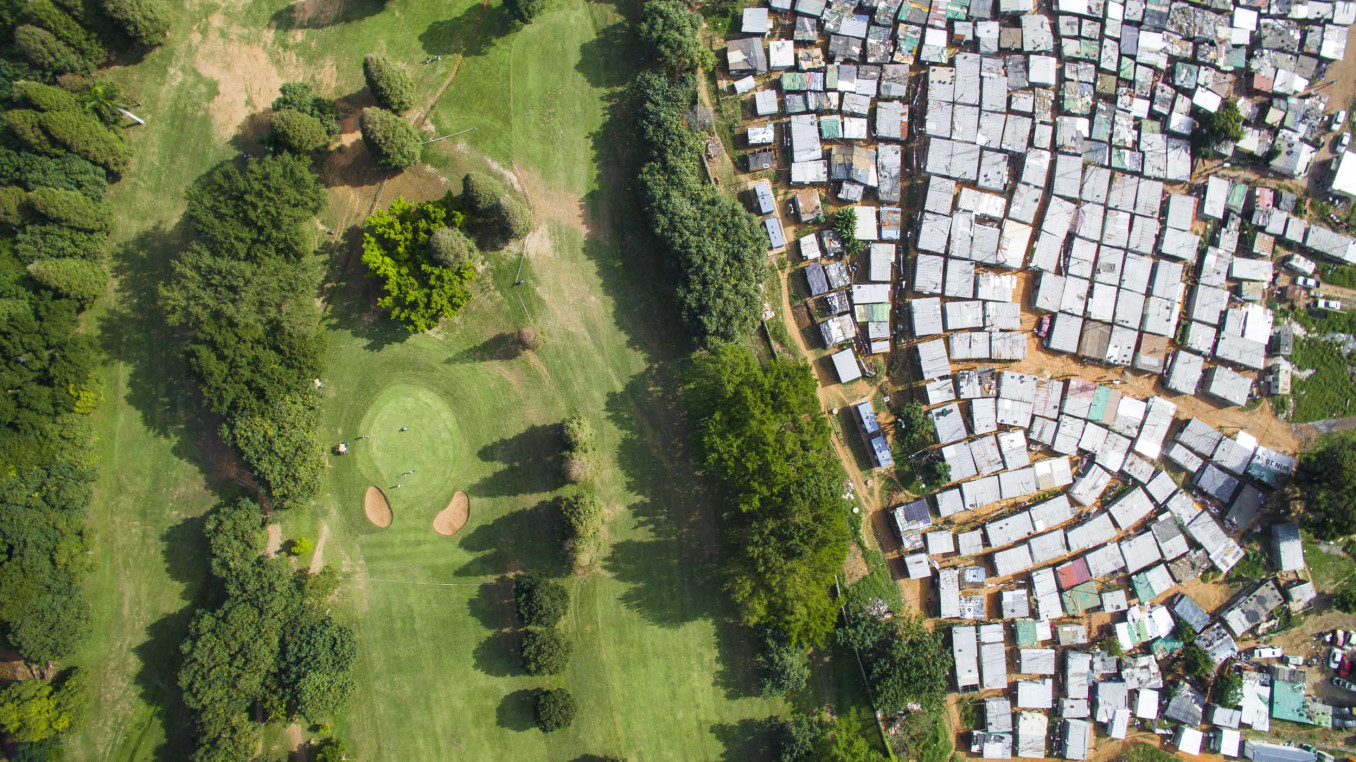A green golf course with a sprawling informal settlement next to it. 