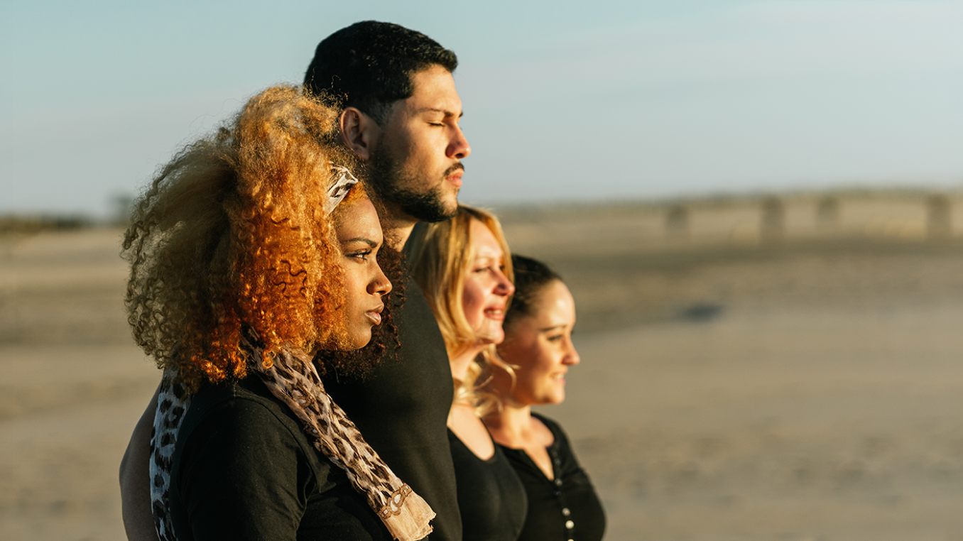 Four people standing and looking at the horizon, with a beach in the background