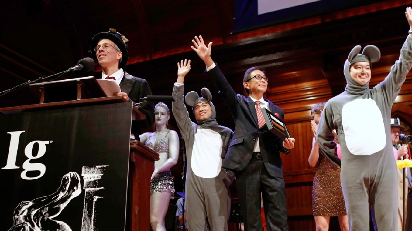 Marc in top hat at podium alongside men dressed as mice and women in silver paint.