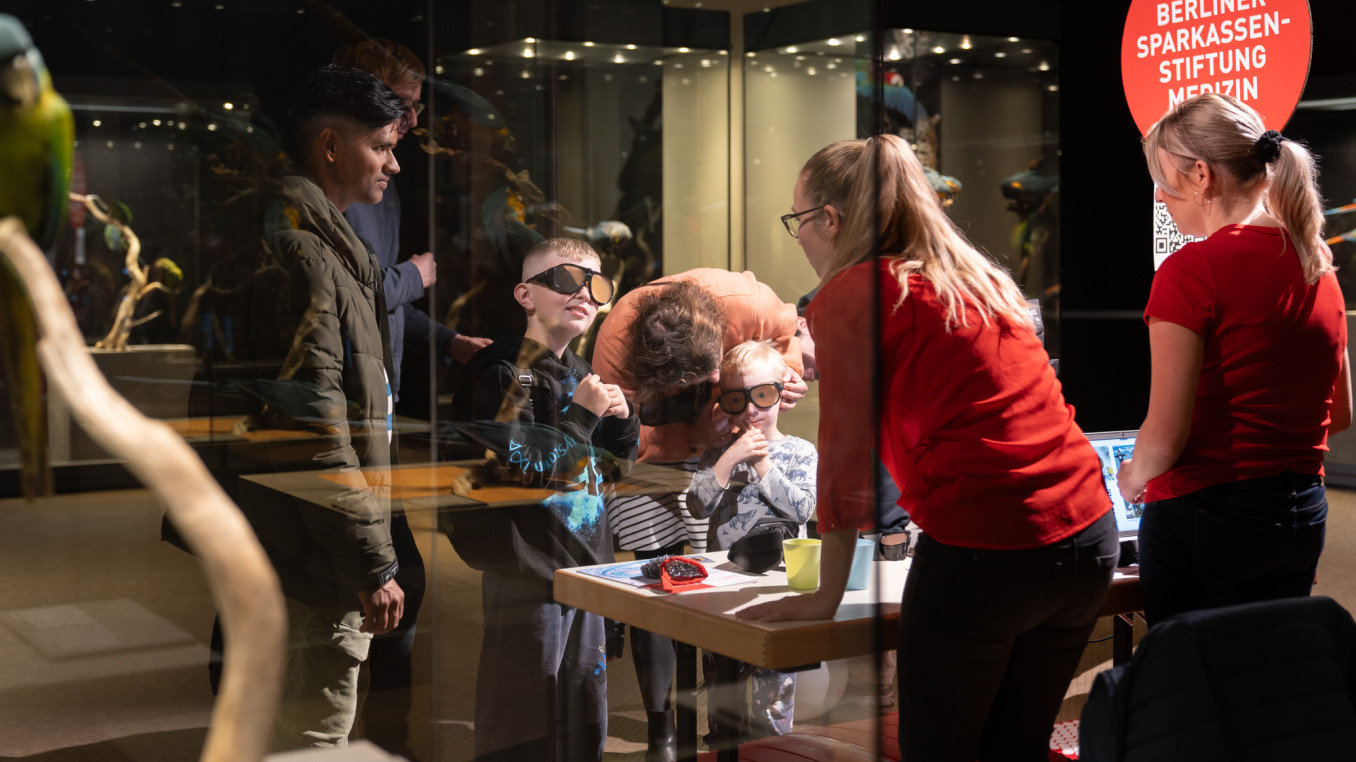 Two children and various adults wear glasses at an exhibition booth.