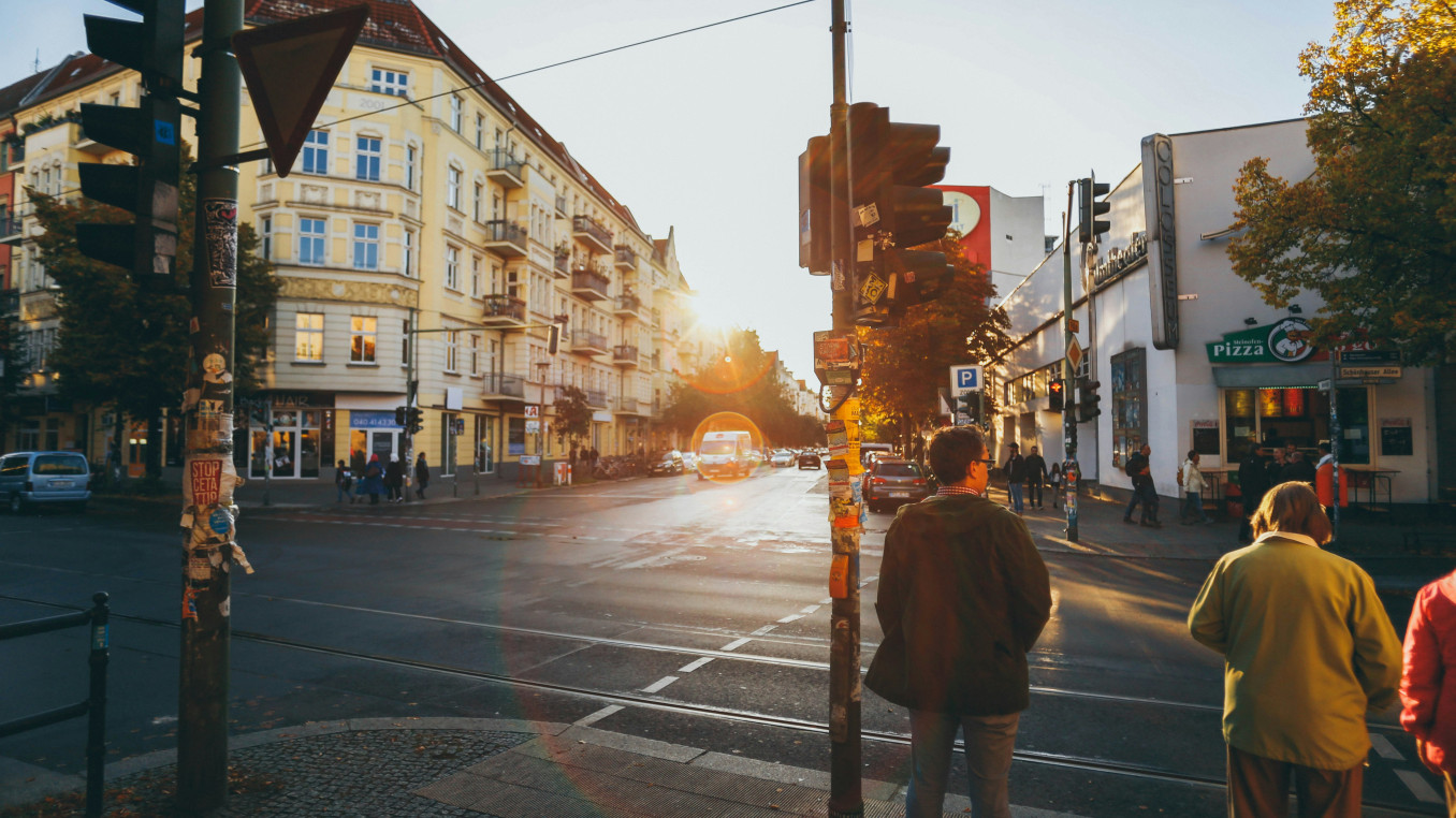 Straßenszene an der Schönhauser Allee mit Fußgängern an einer Ampel und Gebäuden im Hintergrund bei Sonnenuntergang